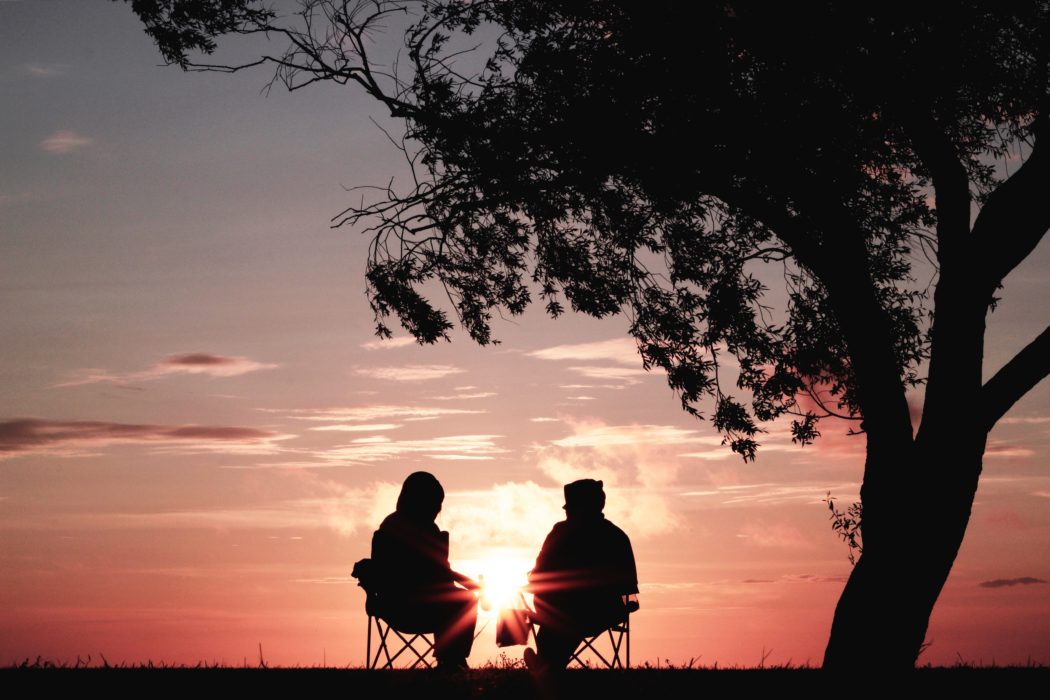 two friends sitting in camp chairs in front of a sunset