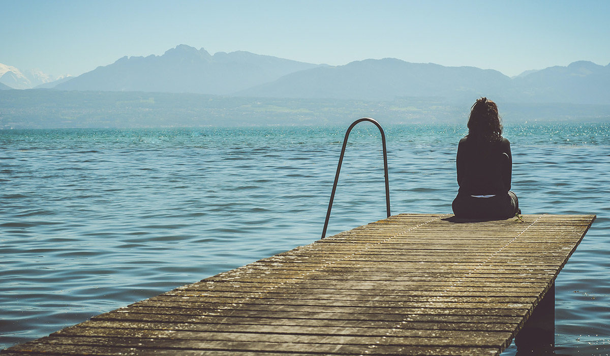 woman sitting at the end of a dock looking out at the water