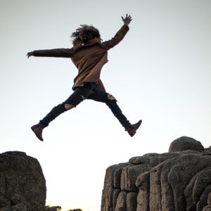 a silhouette of a person jumping between rocks