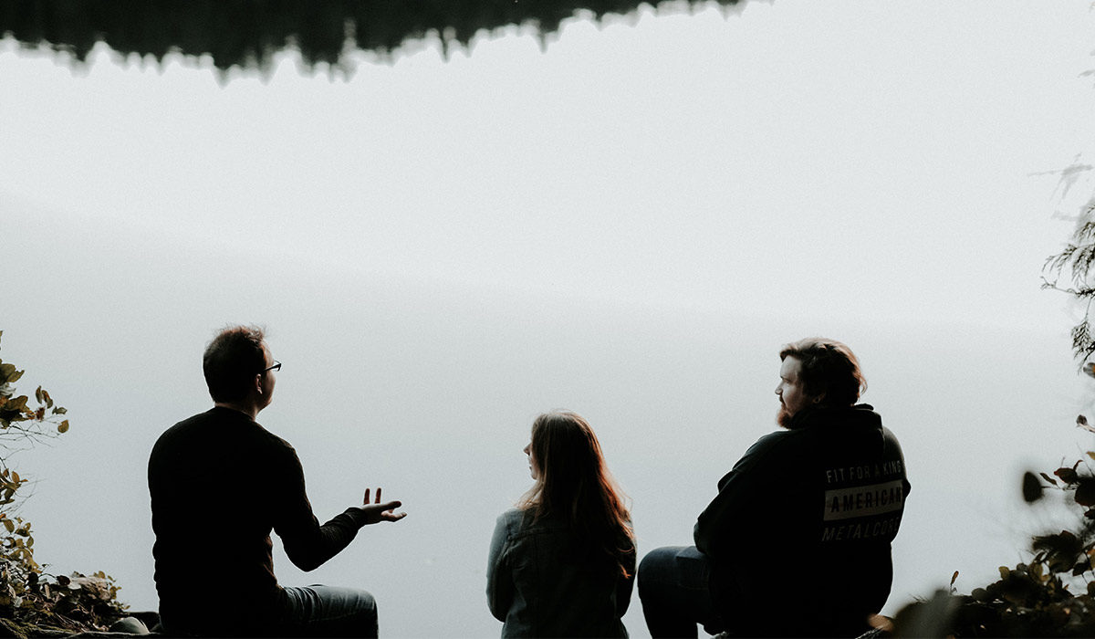 three people sitting at the shore of a lake