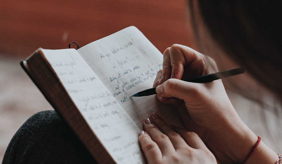 a hand holding a pen and writing in a journal
