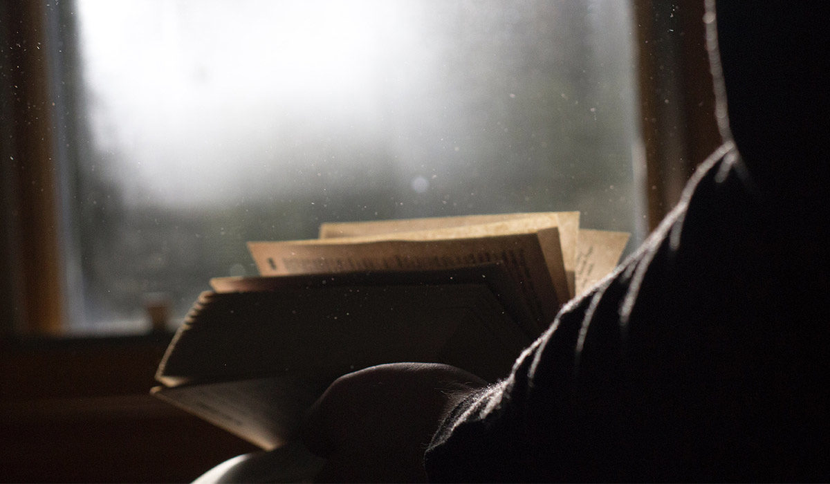 a person holding an open book and looking out the window